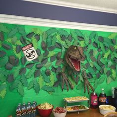 a dinosaur eating food in front of a green wall with paper cutouts on it