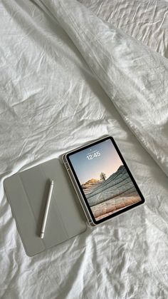 an ipad and pen on a bed with white sheets