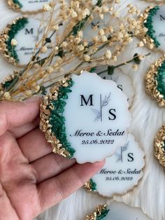 a hand holding a white and green wedding ornament in front of some flowers