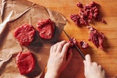 a person cutting up some meat on top of a wooden table next to a knife