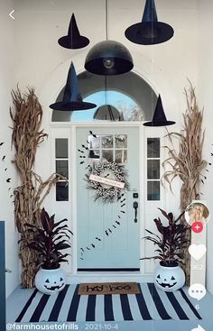 a front door decorated for halloween with pumpkins and plants on the porch, along with two large black hanging lights