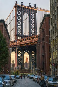 cars are parked on the street in front of tall buildings and a large bridge over it