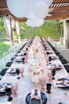 a long table is set with pink and white flowers, black plates, and silverware