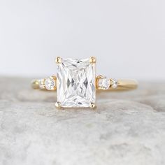 an engagement ring with a princess cut diamond surrounded by three small round brilliant diamonds on top