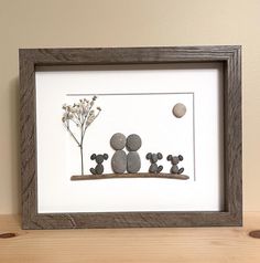 some rocks and flowers in a frame on a wooden table next to a white wall