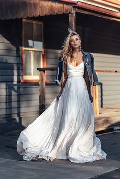 a woman in a white dress and jacket is standing on the side of a building