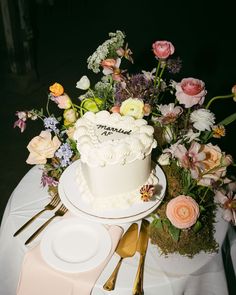 a white cake sitting on top of a table covered in flowers and greenery next to silverware