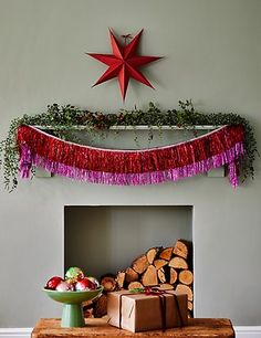 a christmas decoration with red and purple streamers hanging from the ceiling over a fireplace