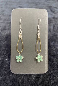 a pair of green and gold earrings with flowers hanging from the end of each ear