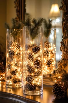 pine cones are placed in glass vases with christmas lights on the mantle behind them