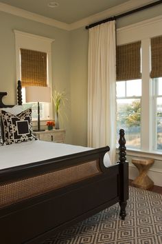 a large bed sitting next to two windows in a room with white curtains and pillows