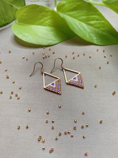 Immerse yourself in the regal allure of our 'Lilac Majesty Triangle Earrings'. Handcrafted with love and precision, each earring features a Stainless Steel Gold link that anchors a royal blend of purple lilac hues, a touch of pristine white and luxurious gold Miyuki beads. Utilizing the ancient technique of bead weaving, specifically brick stitch, this modern design captures the essence of regal sophistication. The gracefully shaped triangles elevate your style, creating an accessory that whispe Handmade Purple Chandelier Earrings As Gift, Purple Drop Chandelier Earrings As Gift, Handmade Purple Earrings For Celebration, Purple Drop Earrings With Dangling Beads, Purple Chandelier Earrings With Ear Wire As A Gift, Lavender Earrings With Dangling Beads For Gifts, Handmade Purple Earrings For Festive Occasions, Nickel-free Purple Chandelier Earrings Gift, Festive Handmade Purple Earrings