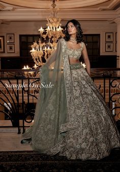 a woman standing in front of a chandelier wearing a green lehenga