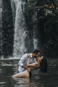 a man and woman are in the water near a waterfall, with their arms around each other