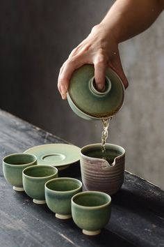 a person pours water from a teapot into small cups on top of a table