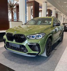 a green bmw suv is on display in a showroom with other cars behind it