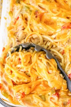 a casserole dish with noodles, cheese and vegetables in it next to a spoon