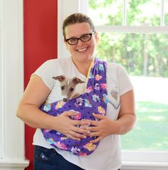 a woman is holding a small dog in her sling while standing next to a window