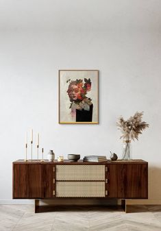 a painting hanging on the wall next to a wooden cabinet with vases and candles