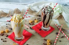 two glasses filled with milkshakes sitting on top of red napkins next to each other