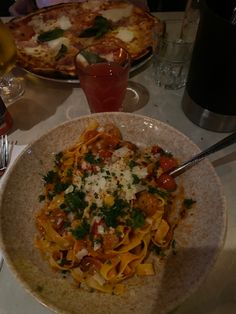 two plates of food are sitting on a table with drinks and pizzas in the background