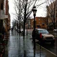 a car parked on the side of a wet street next to a lamp post and trees