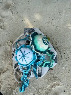 two crocheted items are laying in the sand on top of a beach towel