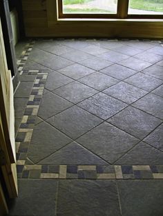 an empty room with tile flooring and windows in the back ground, looking out onto a grassy field