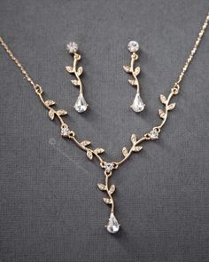 a necklace and earring set with crystal stones on a gray surface, the jewelry is made from gold plated metal