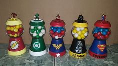 four gummy machines are lined up on a counter top, one is filled with candy and the other has superman's logo