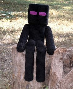 a crocheted black teddy bear sitting on top of a tree stump