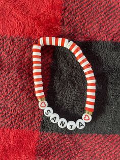 a red and white striped bracelet with name beads on it sitting on top of a blanket