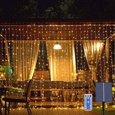 a person holding a remote control in front of a house covered with lights and curtains