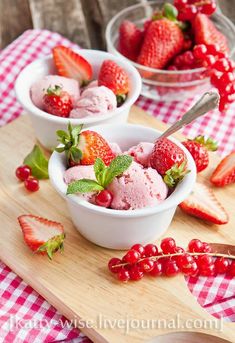 three bowls filled with ice cream and strawberries on top of a wooden cutting board