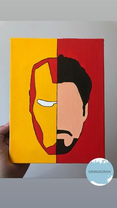 a hand holding up a piece of art with iron man and wolverine face painted on it