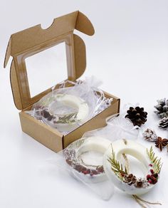 an open box with two white rings and pine cones in it next to other christmas decorations