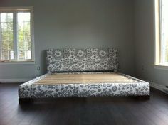 a bed sitting on top of a hard wood floor next to two windows in a room