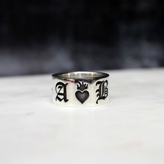 The Sacred Hearts Ring is a beautiful way to honour your love. Customise with you and your loves initials in Old English font either side of a burning sacred heart. The back of the band will be filled with little stars.  This ring makes a stunning alternative wedding band, especially as a set with matching rings for you and you partner. This ring is available in 10mm or 12mm. Wide bands look great on larger finger sizes whilst the 10mm band will be more comfortable for smaller finger sizes.  Ste Personalized Silver Heart Ring For Wedding, Sterling Silver Heart-shaped Engraved Ring, Heart-shaped 14k Stamped Signet Ring For Wedding, Valentine's Day Silver Heart-shaped Engraved Ring, Valentine's Day Heart-shaped Sterling Silver Engraved Ring, Thick Silver Ring, Alternative Wedding Bands, Old English Font, Alternative Wedding Rings