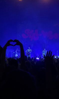 people are holding their hands up in the air as they perform on stage at a concert