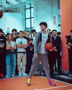 a young man holding a basketball while standing on top of a red floor next to a group of people