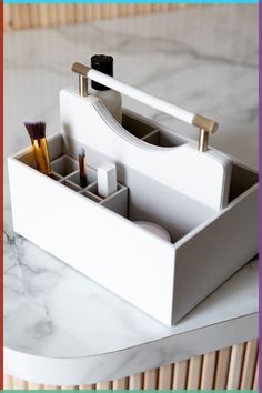 a white desk organizer with two pens and brushes in it on top of a marble table