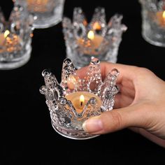 a person holding a crystal crown candle holder in front of several small glass candlesticks