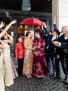 people are throwing confetti on each other in front of a building while the woman is holding an umbrella