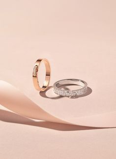 two wedding rings sitting next to each other on top of a pink surface with white ribbons