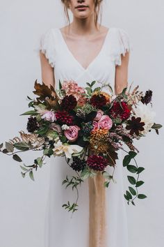 a woman in a white dress holding a large bouquet with red and pink flowers on it