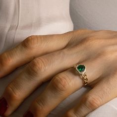 a woman's hand wearing a ring with a green stone on it and red nails