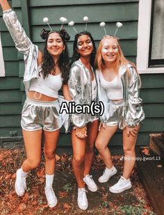 three girls in silver outfits posing for the camera with their arms up and one girl wearing white