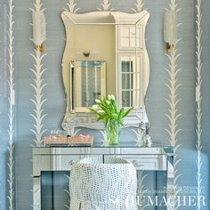 a vanity with a mirror, stool and vase on it in front of a wallpapered background