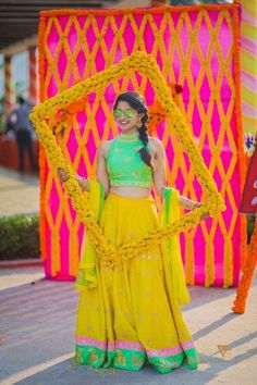 a woman in a yellow and green lehenga standing next to a colorful backdrop