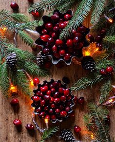 pine cones and cranberries are surrounded by christmas lights on a wooden table with evergreen branches